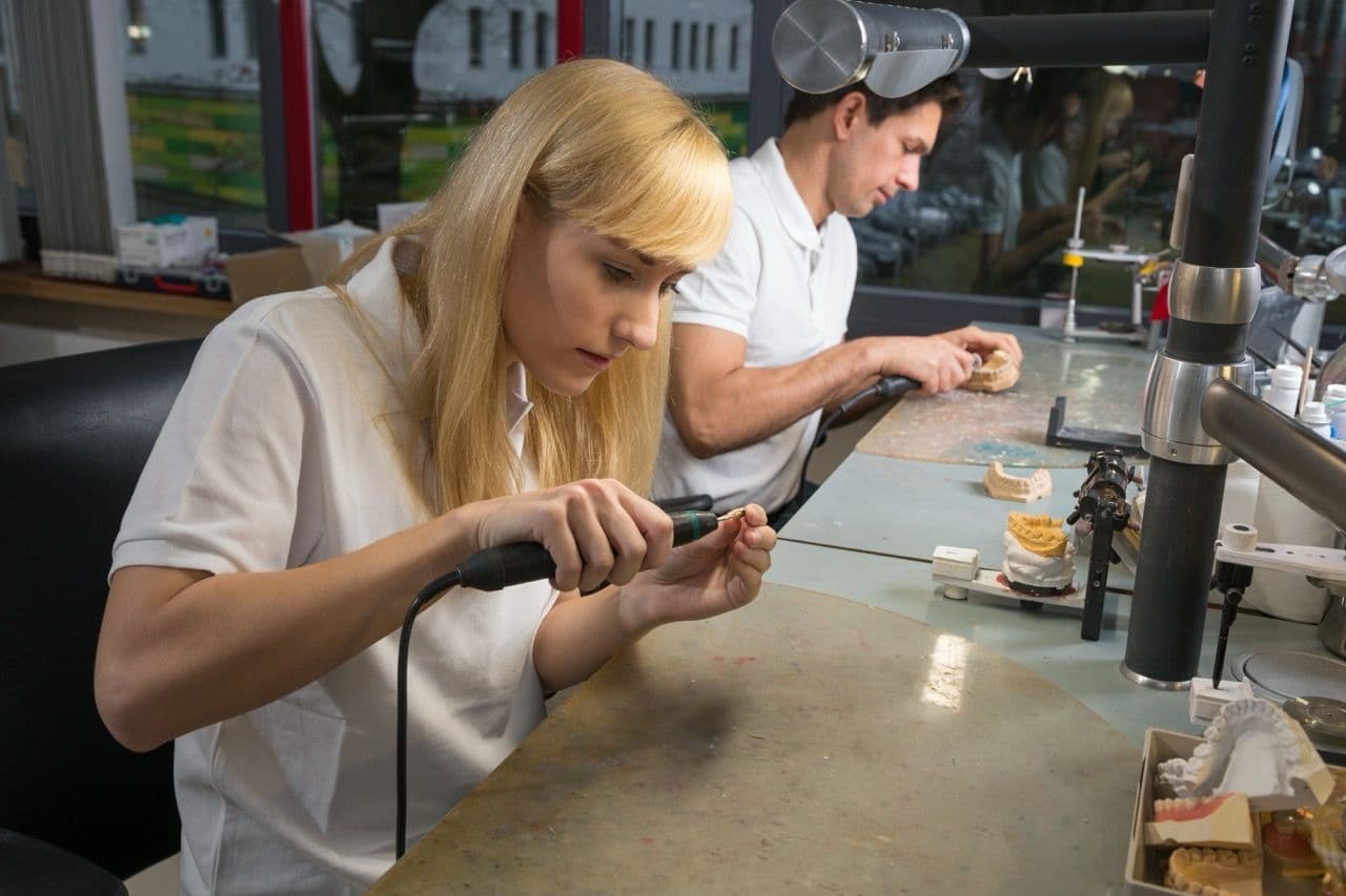 Photo of two people working on gold crowns in a lab.