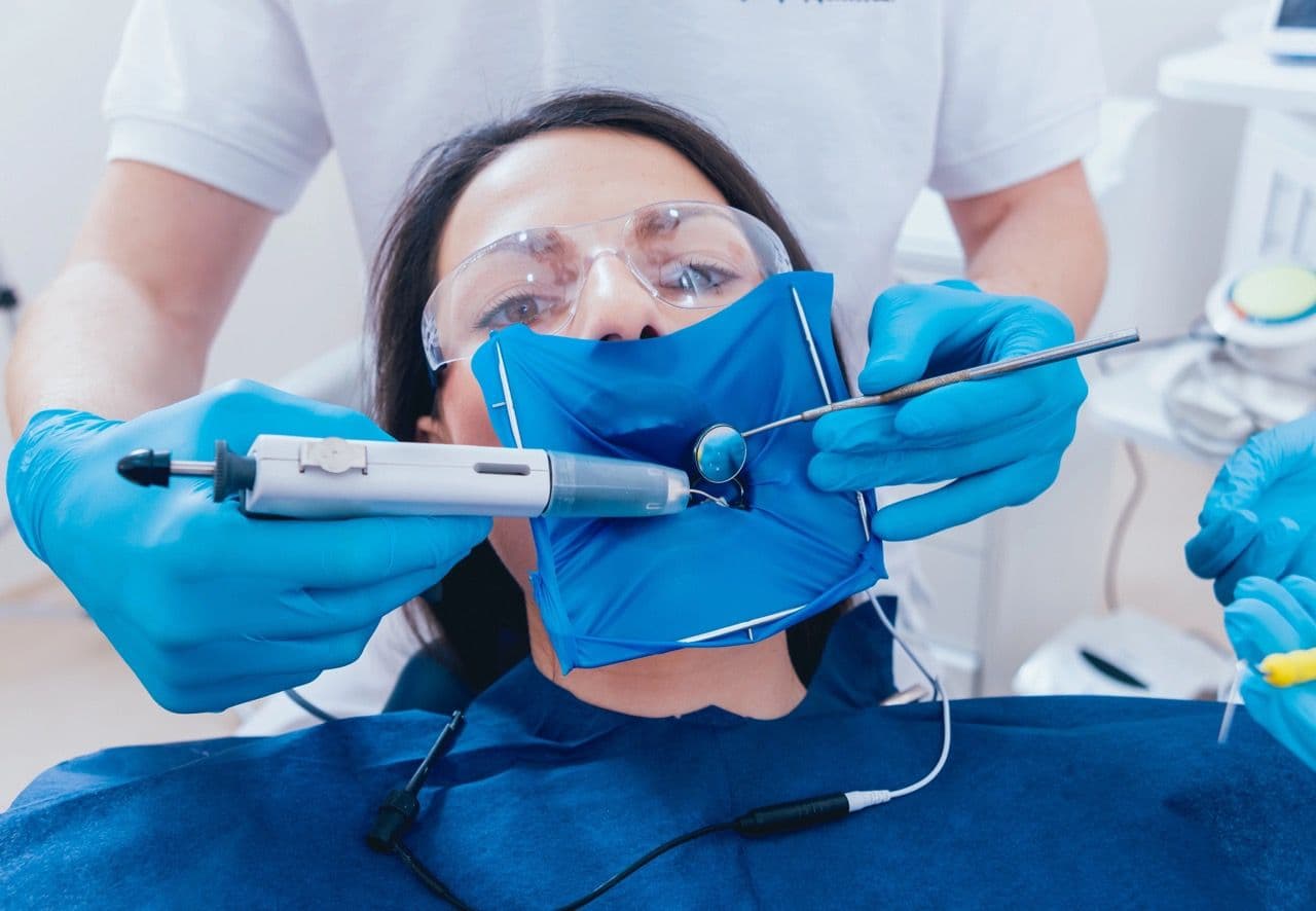 Photo of a root canal patient with tools in her mouth