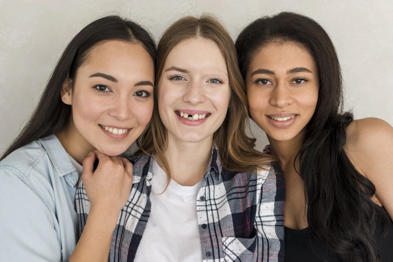 Photo of three young women smiling with one missing a tooth