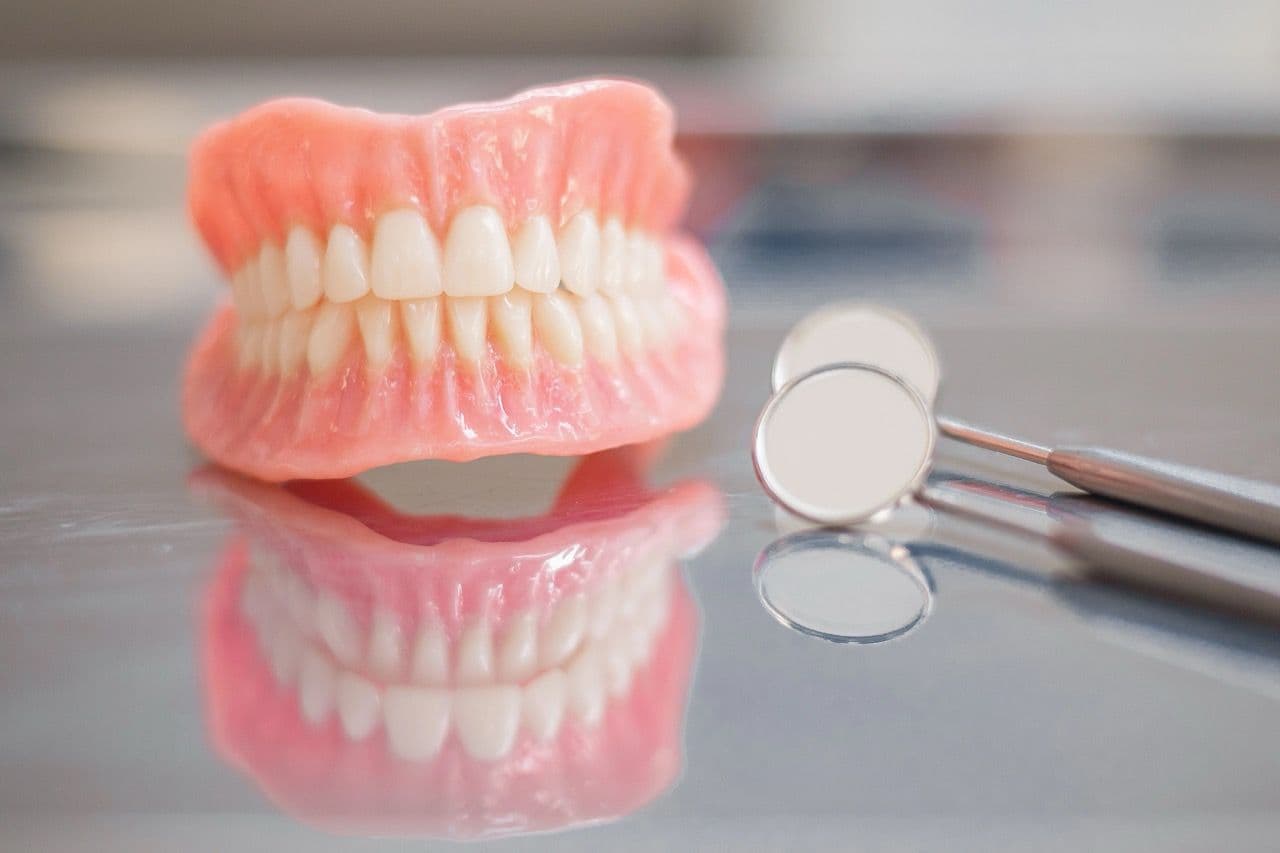 Photo of a full denture set on a table by a mirror instrument